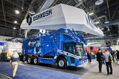 CES attendees walk around a blue McNeilus Volterra ZDL electric refuse and collection vehicle in the Oshkosh Corporation booth.