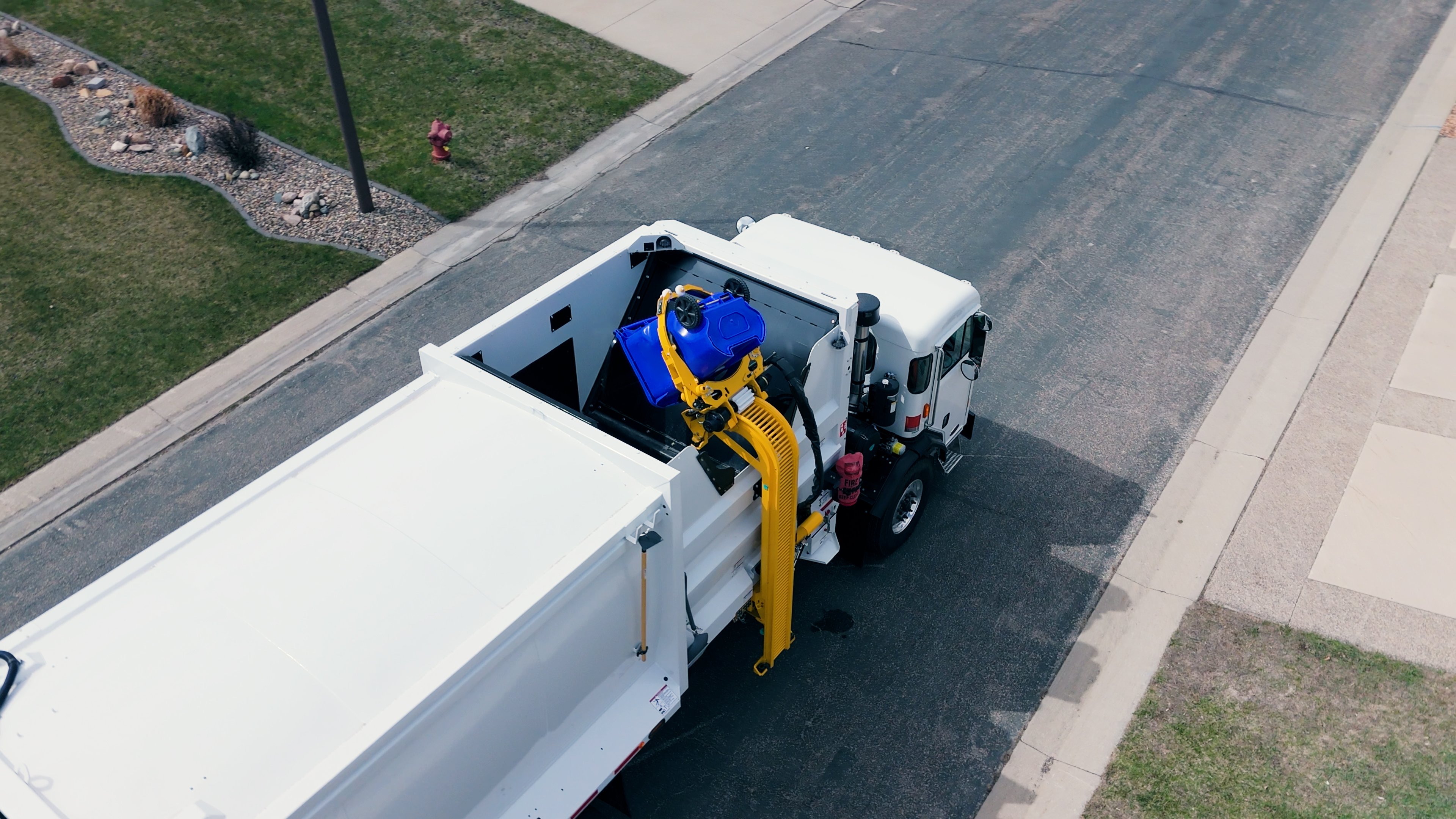 An aerial view of a garbage truck arm dumping a garbage can into the truck.