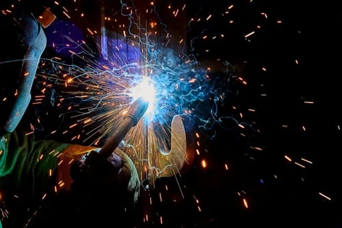 An industrial welder creates sparks while fabricating metal parts for refuse truck manufacturing.