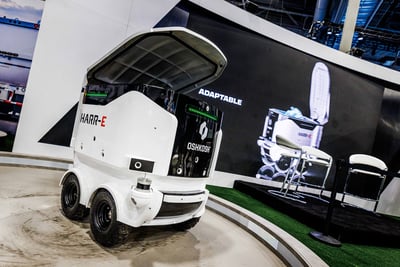 A white electric refuse and recycling collection robot is featured on the show floor at CES in the Oshkosh Corporation booth.