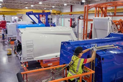 An assembly line inside an industry 4.0 manufacturing facility shows an employee working on the top of vehicle parts, with other vehicle parts in side-by-side stations along the line.