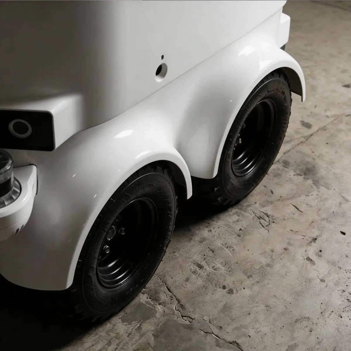 Close-up of the HARR-E autonomous electric refuse robot's rear wheels and white chassis on a concrete floor.