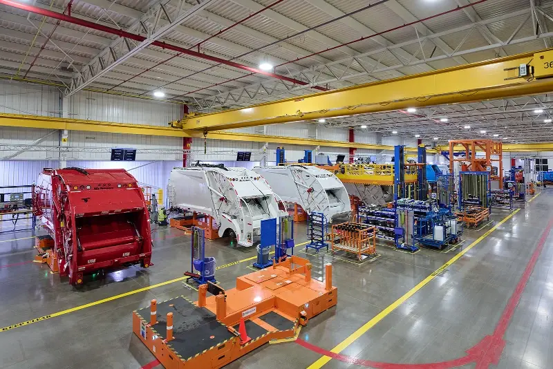 McNeilus refuse truck bodies on a high-flow assembly line inside a modern advanced manufacturing facility.